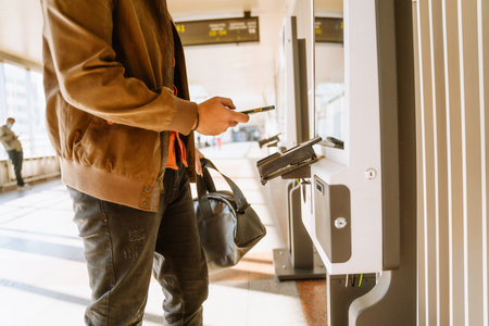 Indian man buying ticket with cellphone at train station indoorsの写真素材