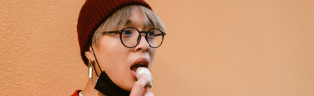 Asian boy wearing eyeglasses eating cookie while standing by wall outdoors