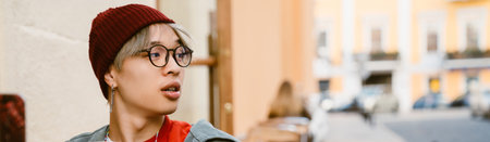 Asian boy in eyeglasses looking aside while sitting at cafe outdoorsの写真素材
