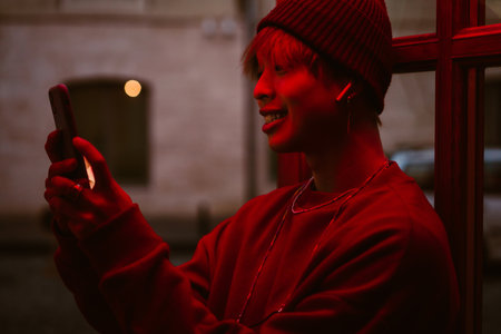 Asian boy using cellphone and earphones while standing in doorway