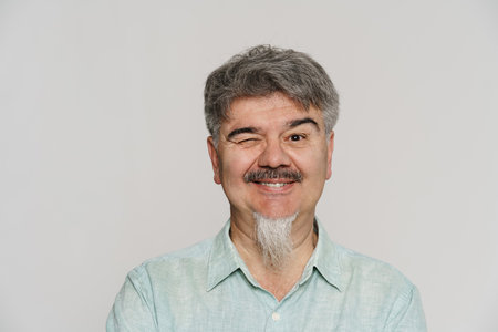 Mature man with grey beard smiling and winking at camera isolated over white background