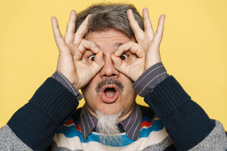 Mature man expressing surprise and showing ok sign isolated over yellow backgroundの写真素材