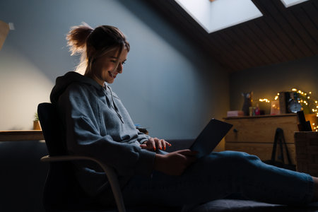 White girl with tunnel rings using laptop while sitting in armchair at homeの写真素材