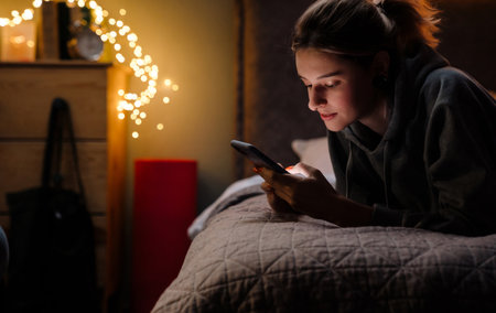 White girl using mobile phone while resting on bed at homeの写真素材