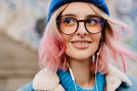 Young woman in eyeglasses smiling and listening music while standing outdoorsの写真素材
