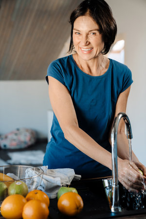 White mature woman washing fruits while cooking in kitchen at homeの写真素材