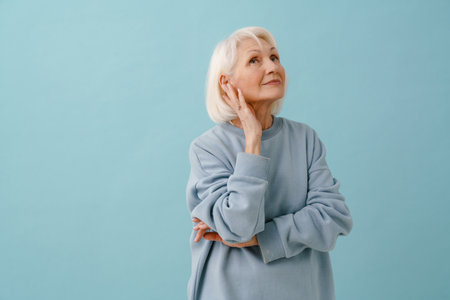 Beautiful thoughtful senior woman in blue pullover looking upward over isolated blue backgroundの写真素材