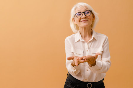 Beautiful senior woman in business suit and glasses showing empty hands over isolated brown backgroundの写真素材