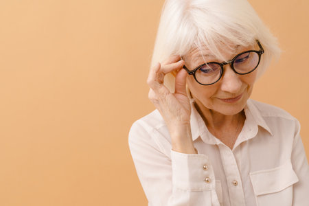Beautiful senior woman in white shirt adjusting her glasses over isolated brown backgroundの写真素材