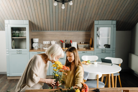 White senior woman making bouquet with her granddaughter in kitchen at homeの写真素材