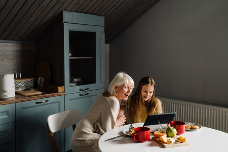 Senior woman and her granddaughter using tablet computer while having breakfast at homeの写真素材