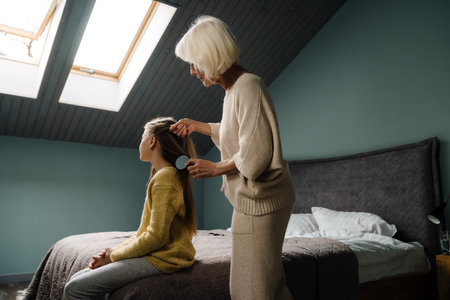 Happy senior woman making hairstyle to her granddaughter at homeの写真素材