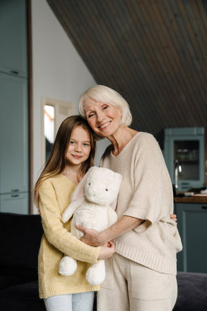 Happy grandmother and granddaughter hugging while posing with toy at homeの写真素材