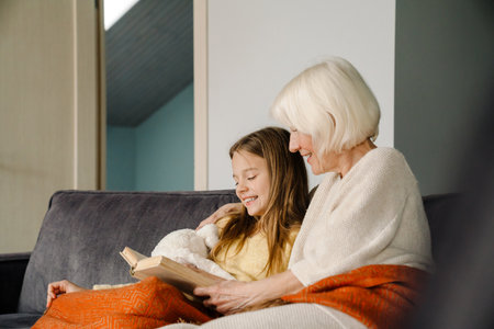 White girl reading book with her grandmother while siting on couch at homeの写真素材
