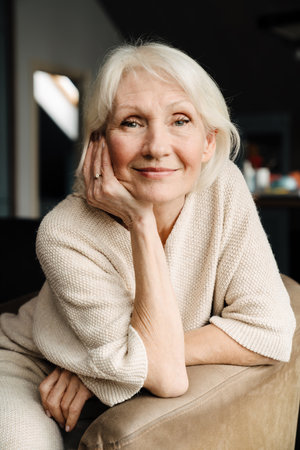 White senior woman smiling and looking at camera while sitting in armchair at home