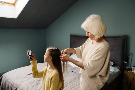 White mature woman doing granddaughter's hairstyle at homeの写真素材