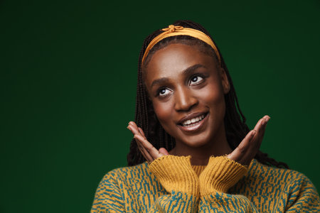 Young black woman wearing headband gesturing and smiling at camera isolated over green wallの写真素材