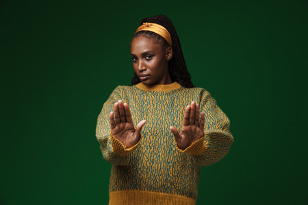 Young black woman wearing headband showing stop gesture isolated over green wall
