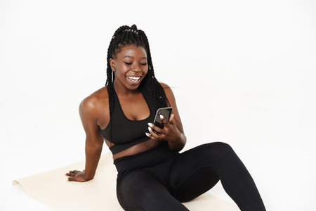 Black young woman using cellphone during yoga practice isolated over white backgroundの写真素材
