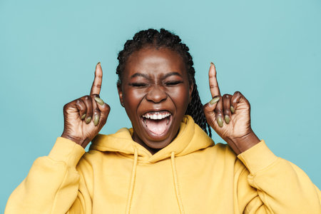 Young black woman laughing and pointing fingers upward isolated over blue background