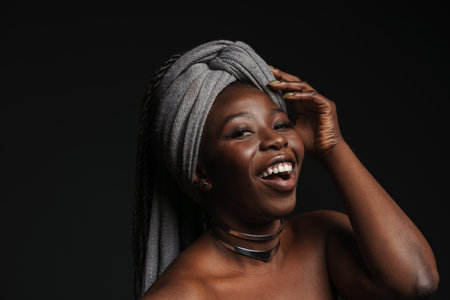 Shirtless black woman wearing headscarf laughing at camera isolated over dark backgroundの写真素材