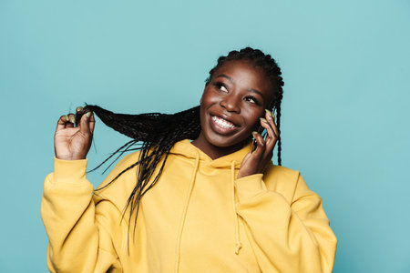 Young black woman wearing hoodie talking on mobile phone isolated over blue backgroundの写真素材