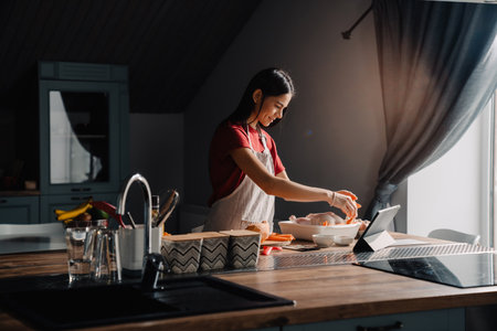 Young hispanic woman using tablet-computer while cooking in kitchen at homeの写真素材