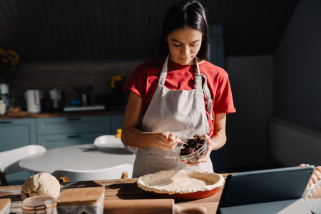Young hispanic woman wearing apron making pie in kitchen at homeの写真素材