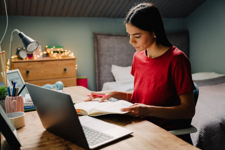 Young hispanic woman writing down notes while working with laptop at homeの写真素材