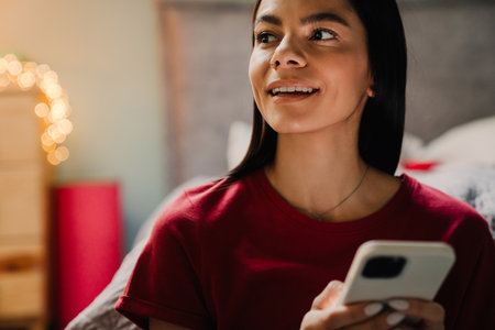Young hispanic woman using cellphone while sitting on floor at homeの写真素材