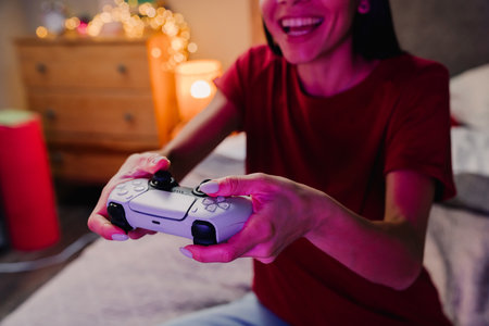 Young hispanic woman smiling and using game controller while sitting on bed at home