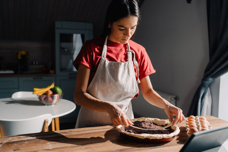 Young hispanic woman wearing apron making pie in kitchen at homeの写真素材