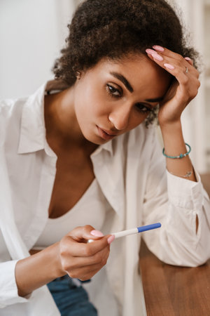 Young black woman being upset while holding pregnancy test at homeの写真素材