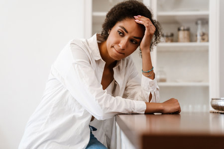 Young black woman being upset and thinking about abortion while sitting on chair at homeの写真素材