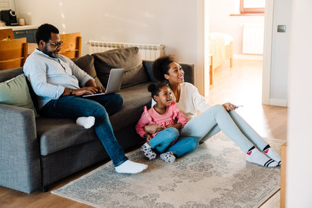 African american family woman and man with little daughter sitting on sofa and watching television at homeの写真素材