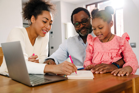 African american family with little girl drawing in notepad with marker while sitting by table at homeの写真素材