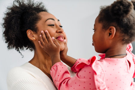 African american happy adult woman smiling and hugging her little daughter at homeの写真素材