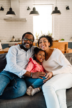 African american family woman and man with little daughter smiling and sitting on sofa at home