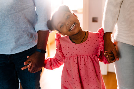 African american family woman and man with little daughter smiling and holding hands at homeの写真素材