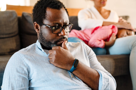 African american woman with little daughter sitting on sofa while man using laptop at homeの写真素材