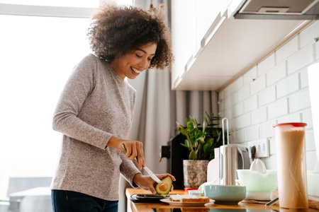 African american young woman with curly afro hairstyle making breakfast in morning at homeの写真素材