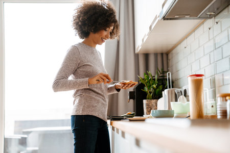 African american young woman with curly afro hairstyle making breakfast in morning at homeの写真素材