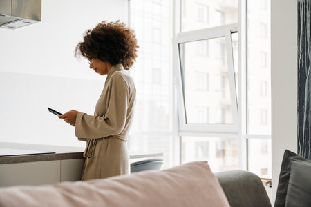 African american young woman with curly hairstyle using cellphone at homeの写真素材