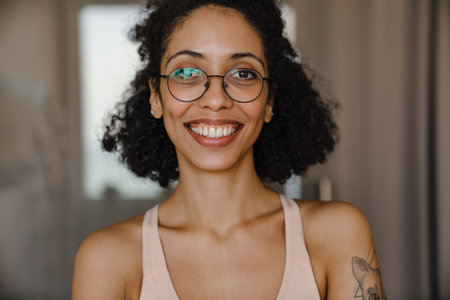 Black young woman wearing eyeglasses smiling while doing workout at homeの写真素材