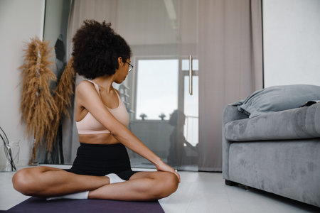 Black woman wearing eyeglasses doing exercise during yoga practice at homeの写真素材