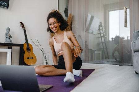 Black young woman wearing eyeglasses using laptop during workout at homeの写真素材