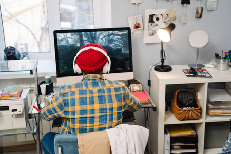 Teenage boy with headphones playing video game on desktop computer at homeの写真素材