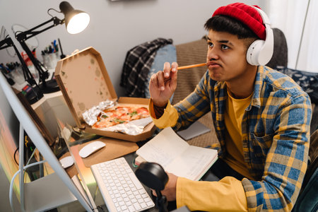 Middle-eastern teenage boy using desktop computer while studying at home