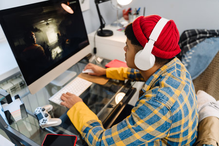 Teenage boy with headphones playing video game on desktop computer at homeの写真素材