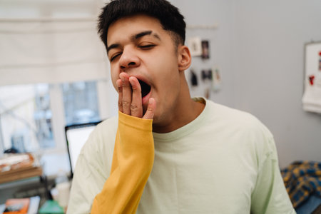 Brunette teenage boy wearing pajama yawning after sleep in bedroomの写真素材